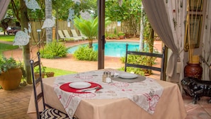A dining area with a table set for two, a pool in the background, and a decorative bull statue. - Destiny Inn Lodge (Polokwane)