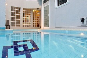 Una piscina con azulejos azules brillantes, suelo de baldosas y acceso por puerta de cristal.