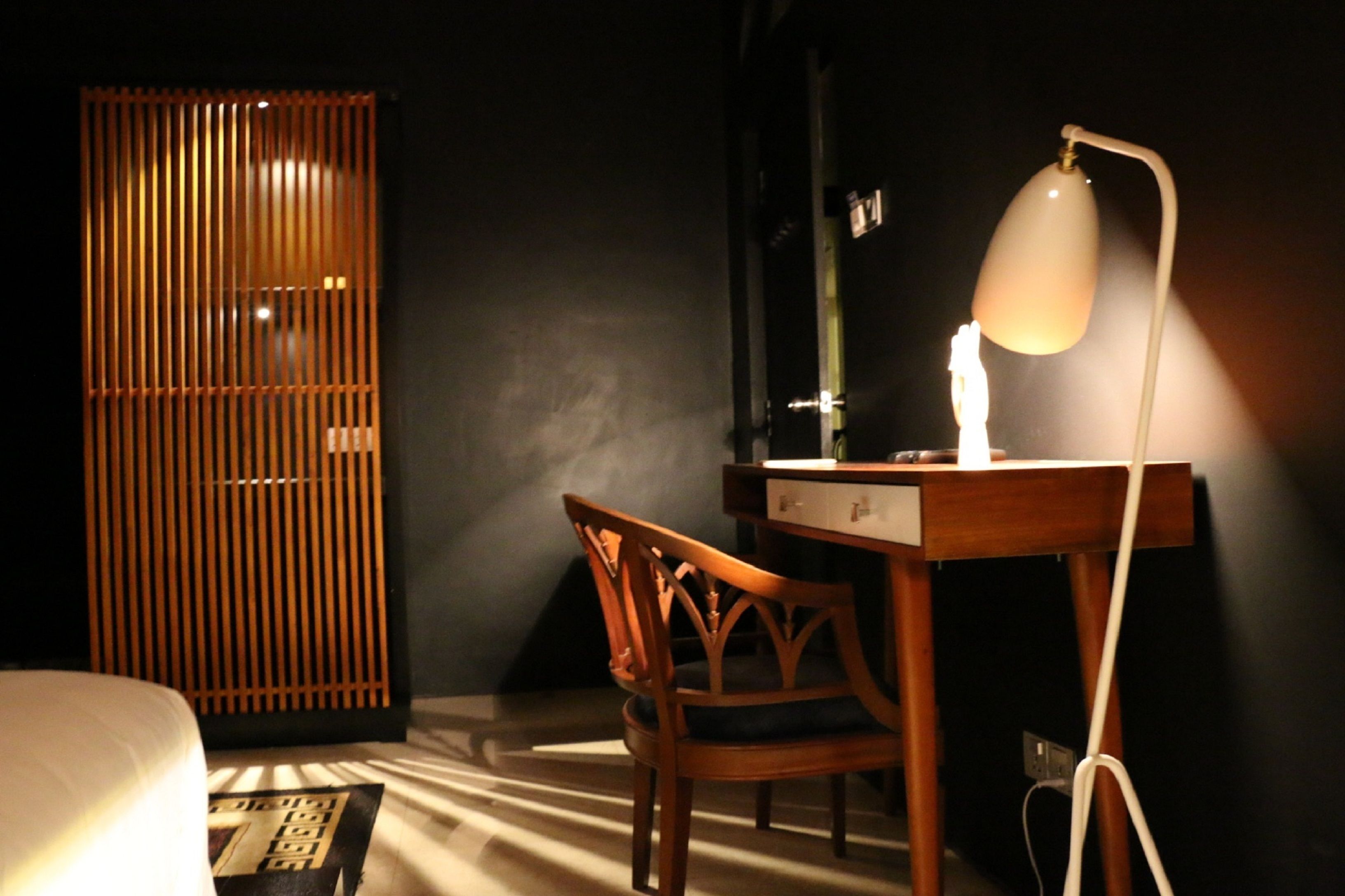 Een zwak verlichte kamer met een houten bureau, een stoel en een lamp.