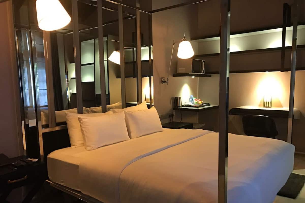 Une chambre d’hôtel avec un grand lit, des tables de chevet, un bureau avec une chaise et un miroir.