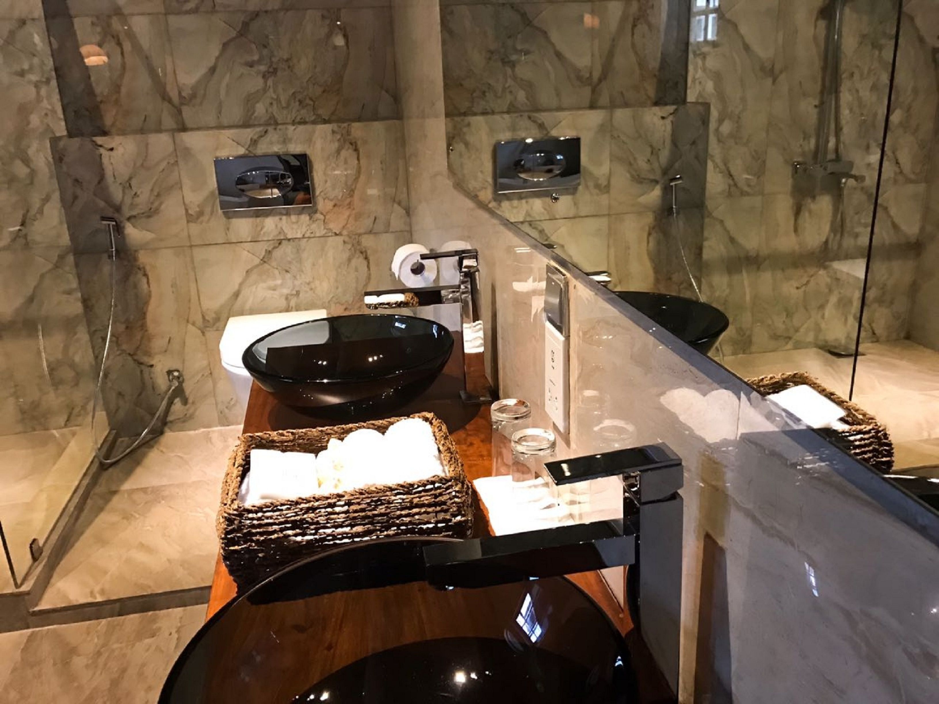 A modern bathroom with a large mirror, a black basin, and a wooden tray with toiletries.