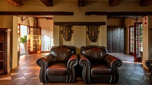 A room with two leather armchairs, wooden beams on the ceiling, and a door with a red frame.