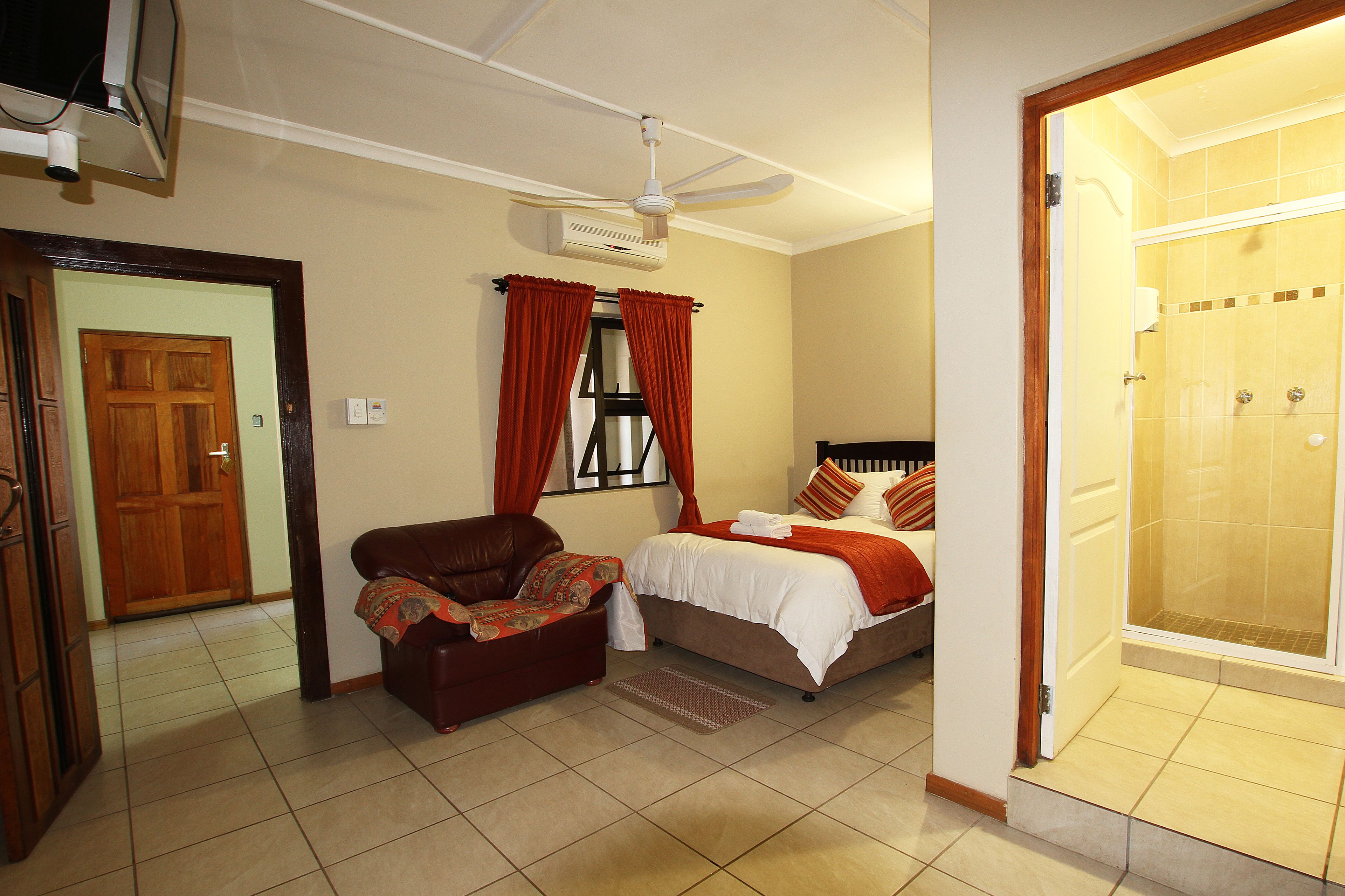 Habitación de hotel con cama, una silla, ventilador de techo, equipo de aire acondicionado y zona de ducha.