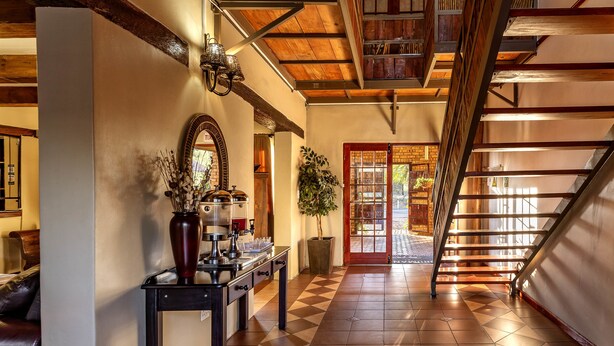 A spacious hallway with a checkered floor, a staircase, a coffee station, and a large mirror.