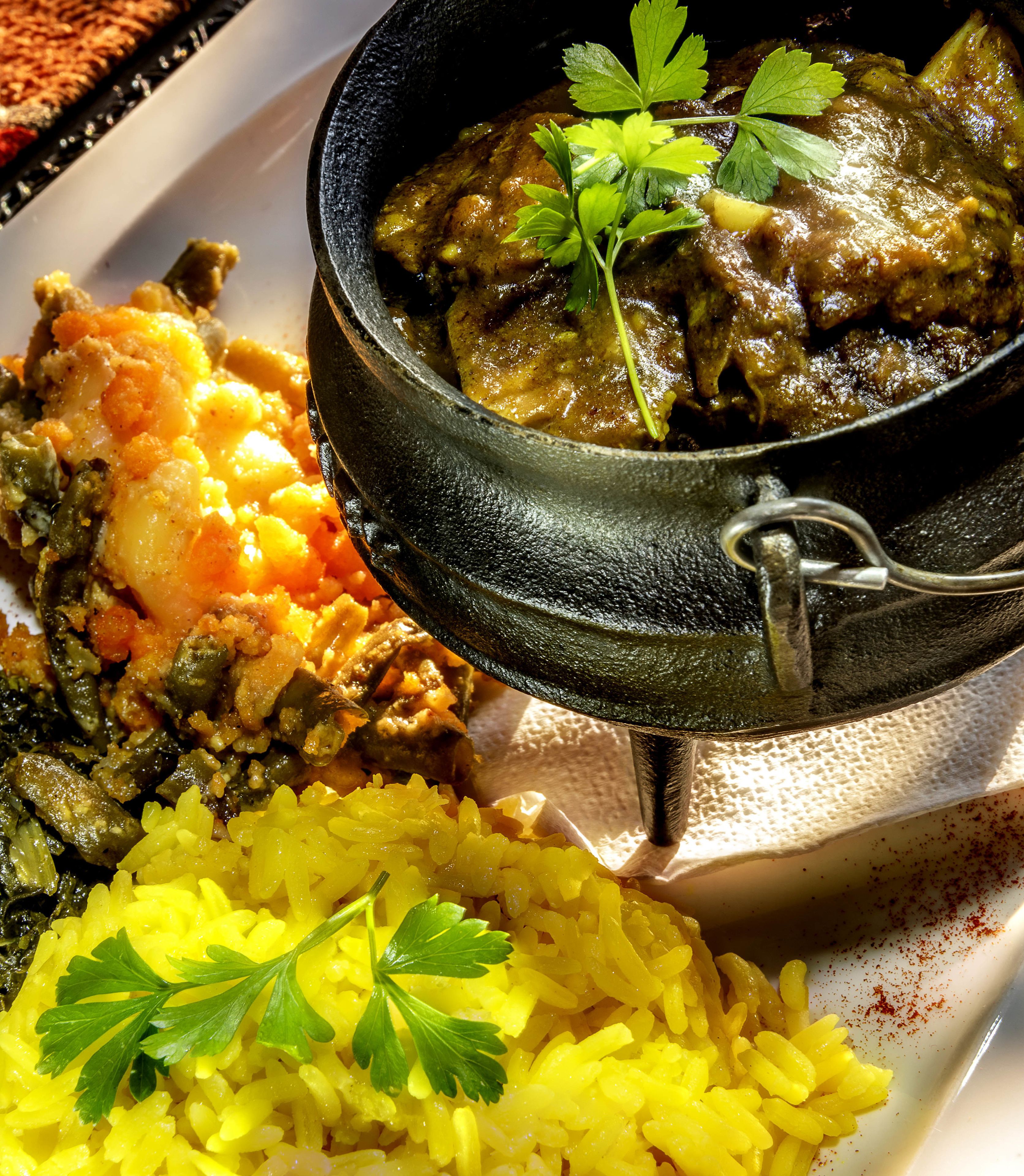Un plato de arroz amarillo adornado con perejil, un cuenco de estofado con carne y vegetales, y una guarnición de puré de papas.