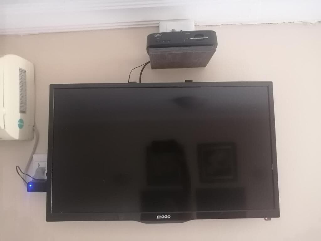 A flat-screen TV mounted on a wall with a power strip and a small device above it.