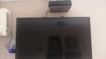 A flat-screen TV mounted on a wall with a power strip and a small device above it.
