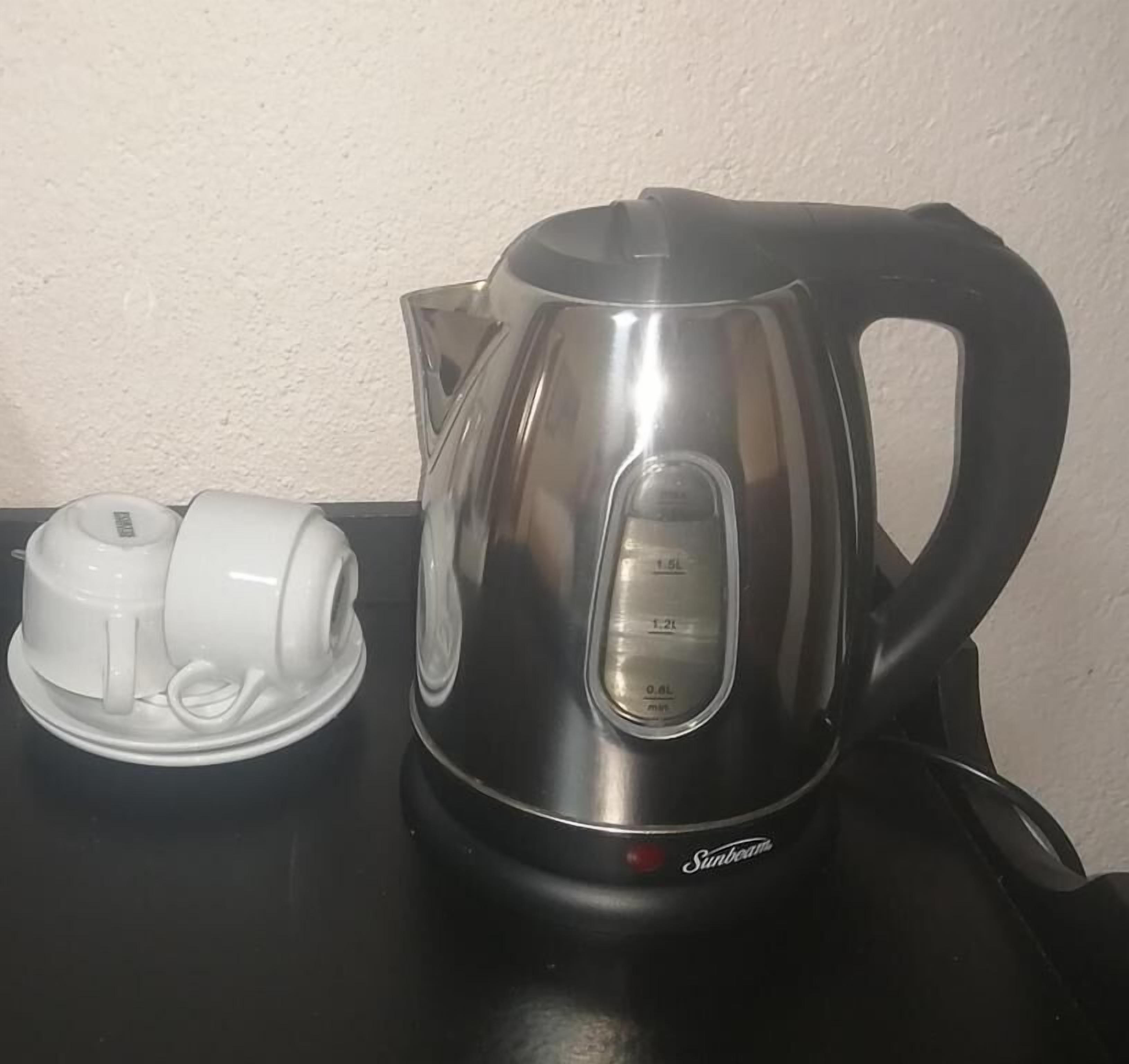 A stainless steel kettle with a digital temperature gauge and a white electric kettle on a black countertop.