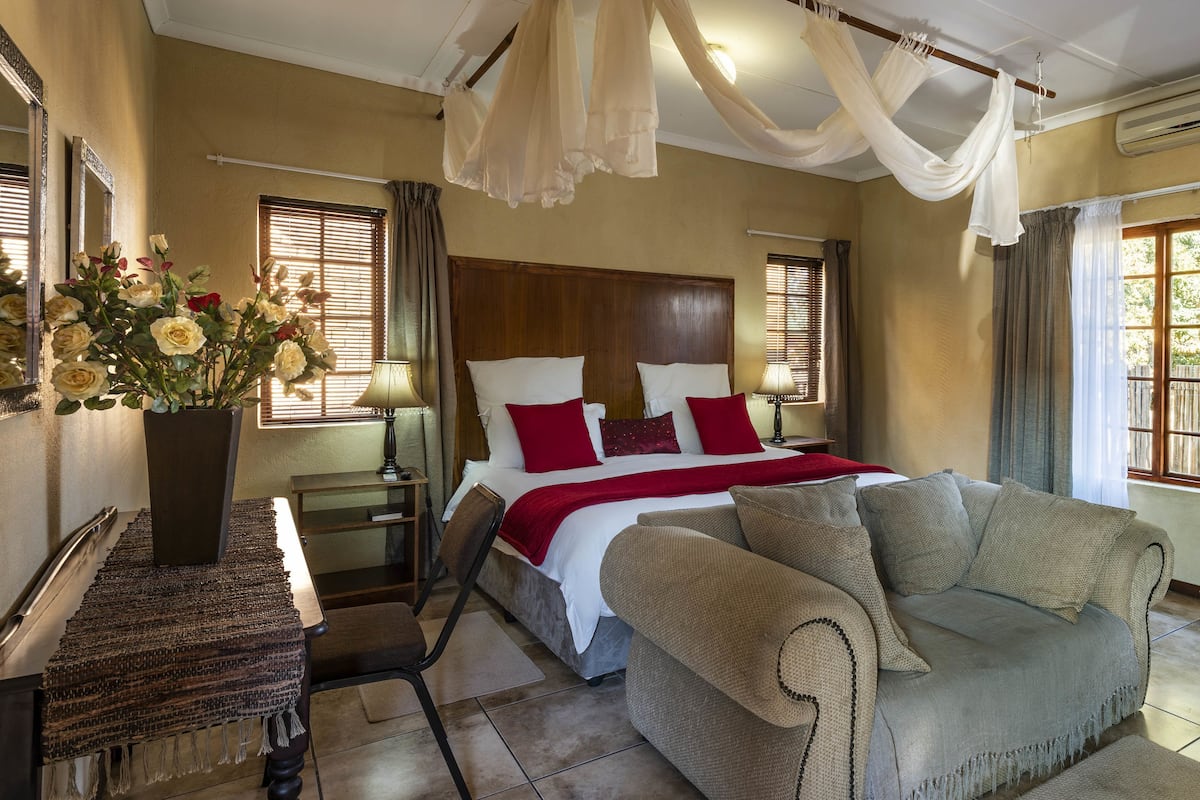 Ein Schlafzimmer mit Bett, Nachttischen, einem Sessel, einem großen Fenster und einer Zimmerpflanze.