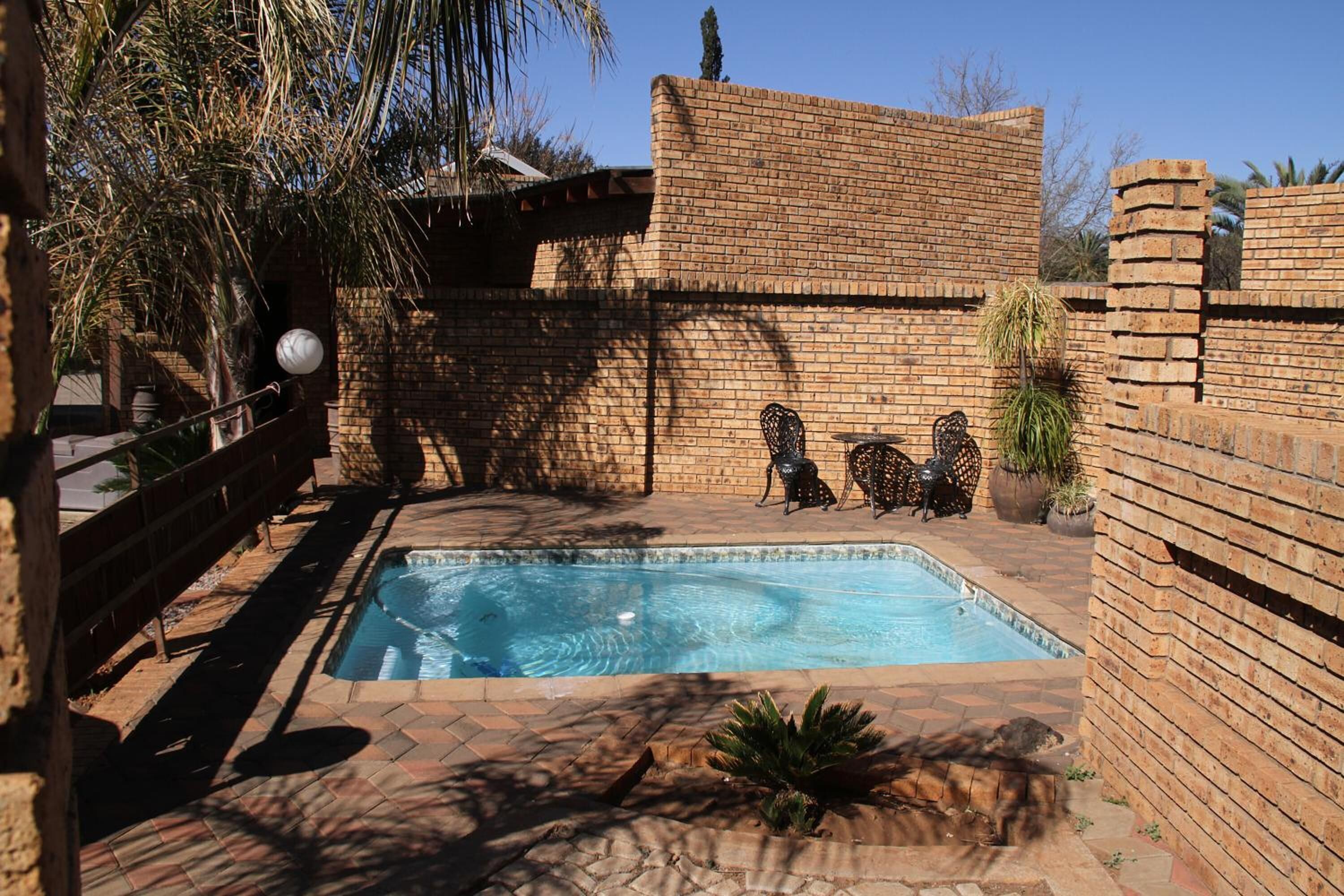 A rectangular swimming pool with a brick wall and a wooden deck surrounding it.