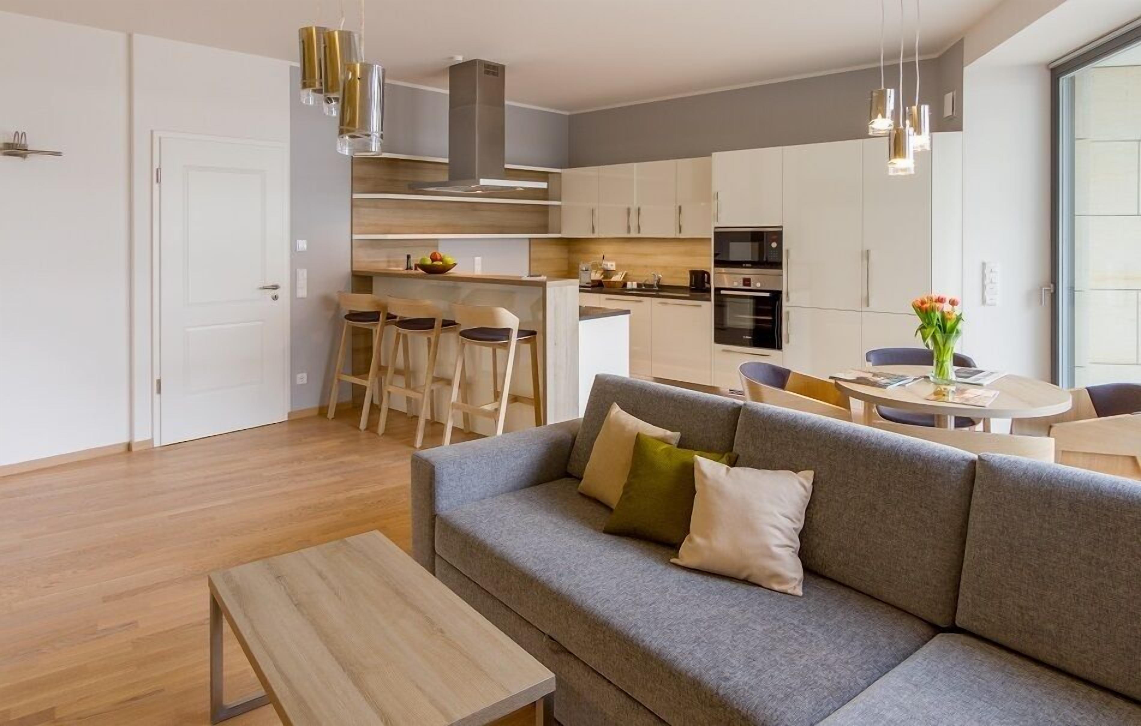 Un appartamento moderno con un divano grigio, un tavolino in legno e un angolo cottura con mobili bianchi e un tavolo da pranzo.