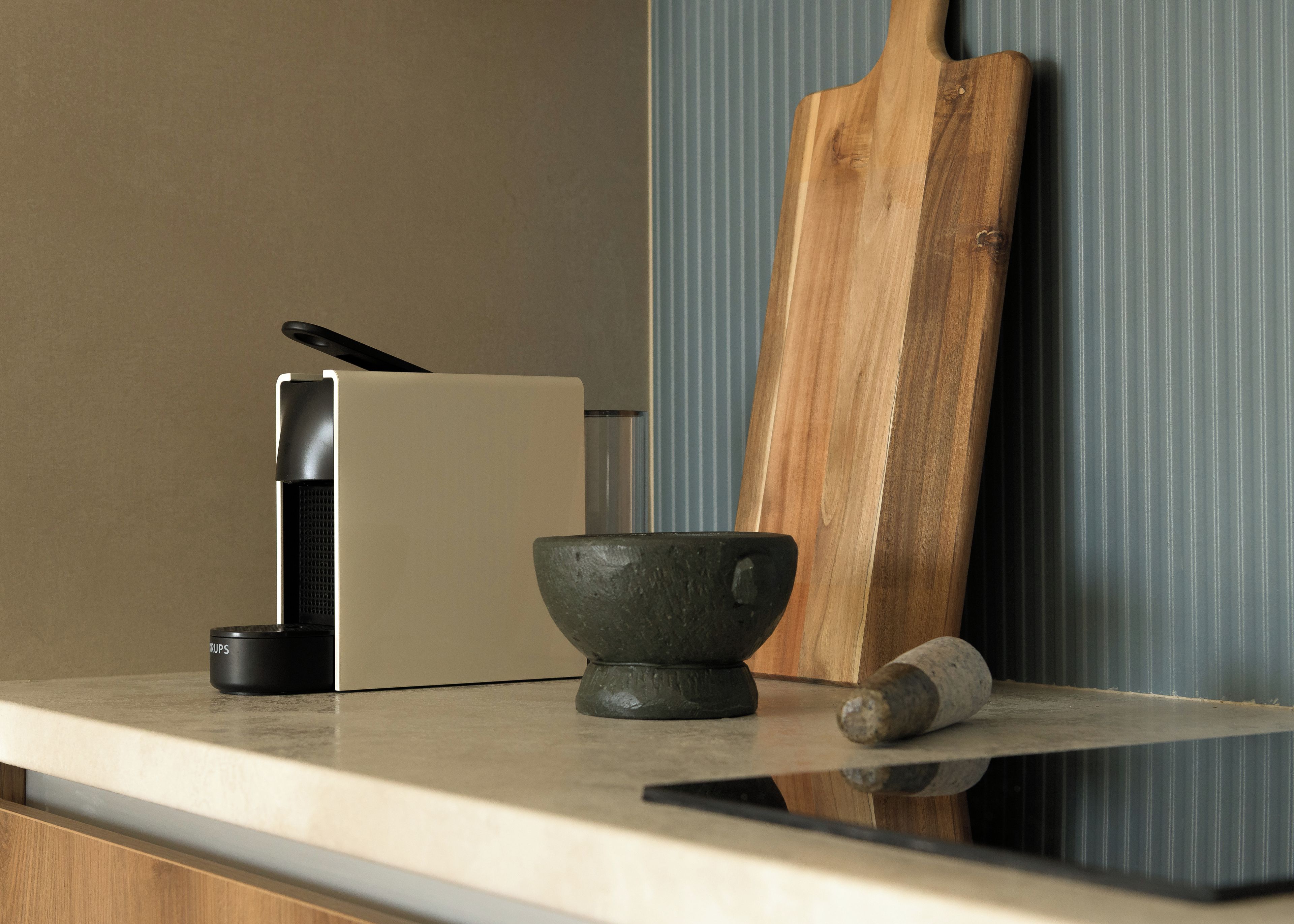 Un plan de travail de cuisine avec une machine à café, un saladier, une planche à découper en bois et un rouleau à pâtisserie.