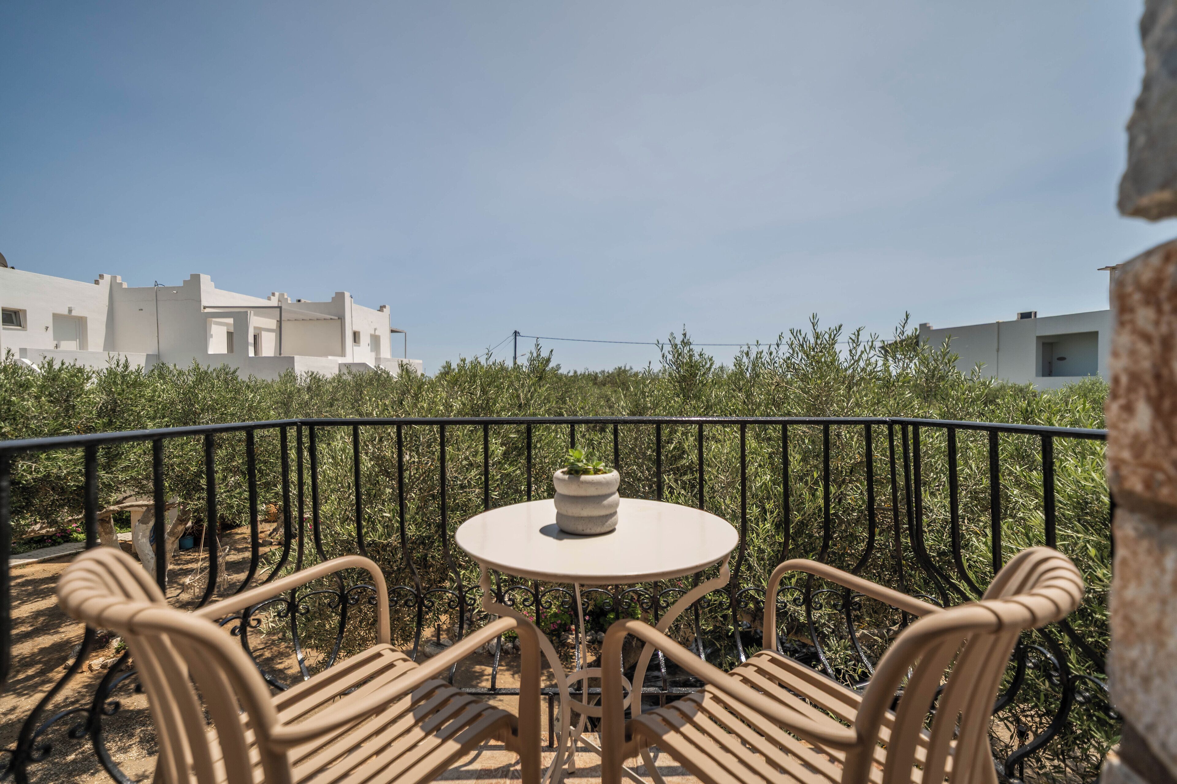 Un balcon avec une table ronde et quatre chaises, une plante en pot posée sur la table, et une vue sur des bâtiments et de la verdure en arrière-plan.
