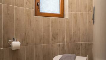 A bathroom with a wooden-framed window, a toilet with a towel, and a toilet paper holder on the wall.