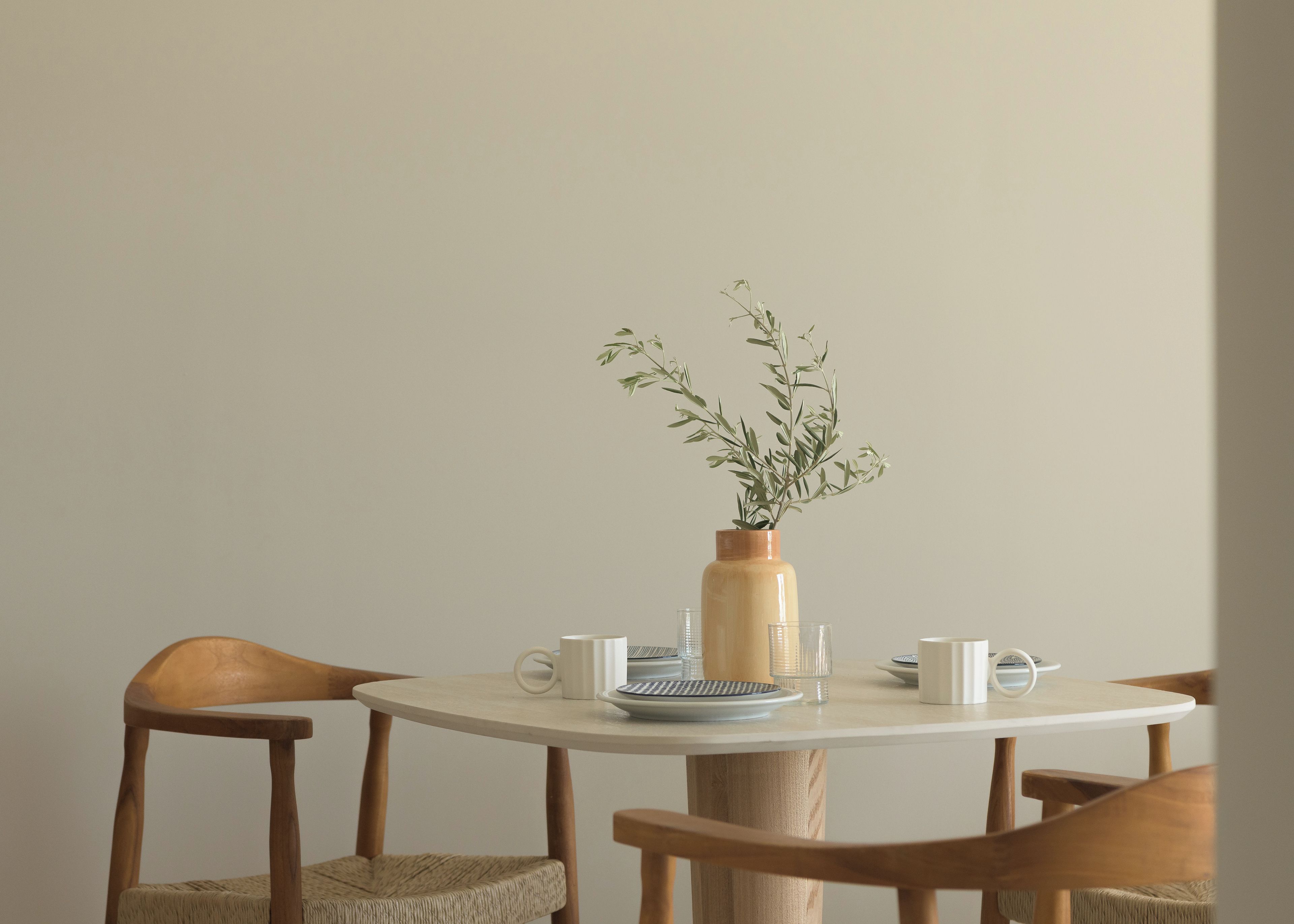 A round table with a vase of green foliage, two white mugs, and a small plate with a spoon.