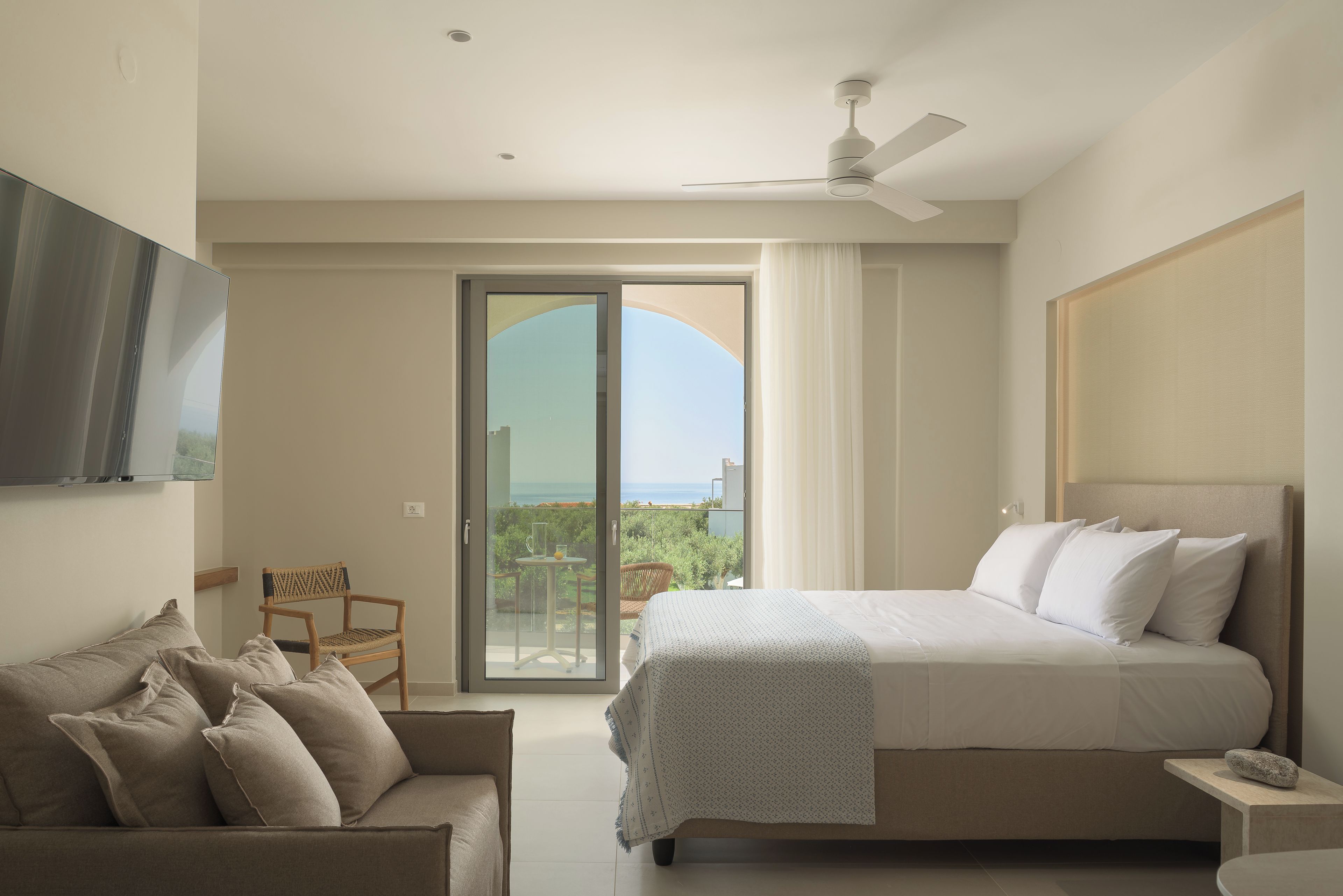 A bedroom with a bed, a sofa, a TV, and a balcony with a view.