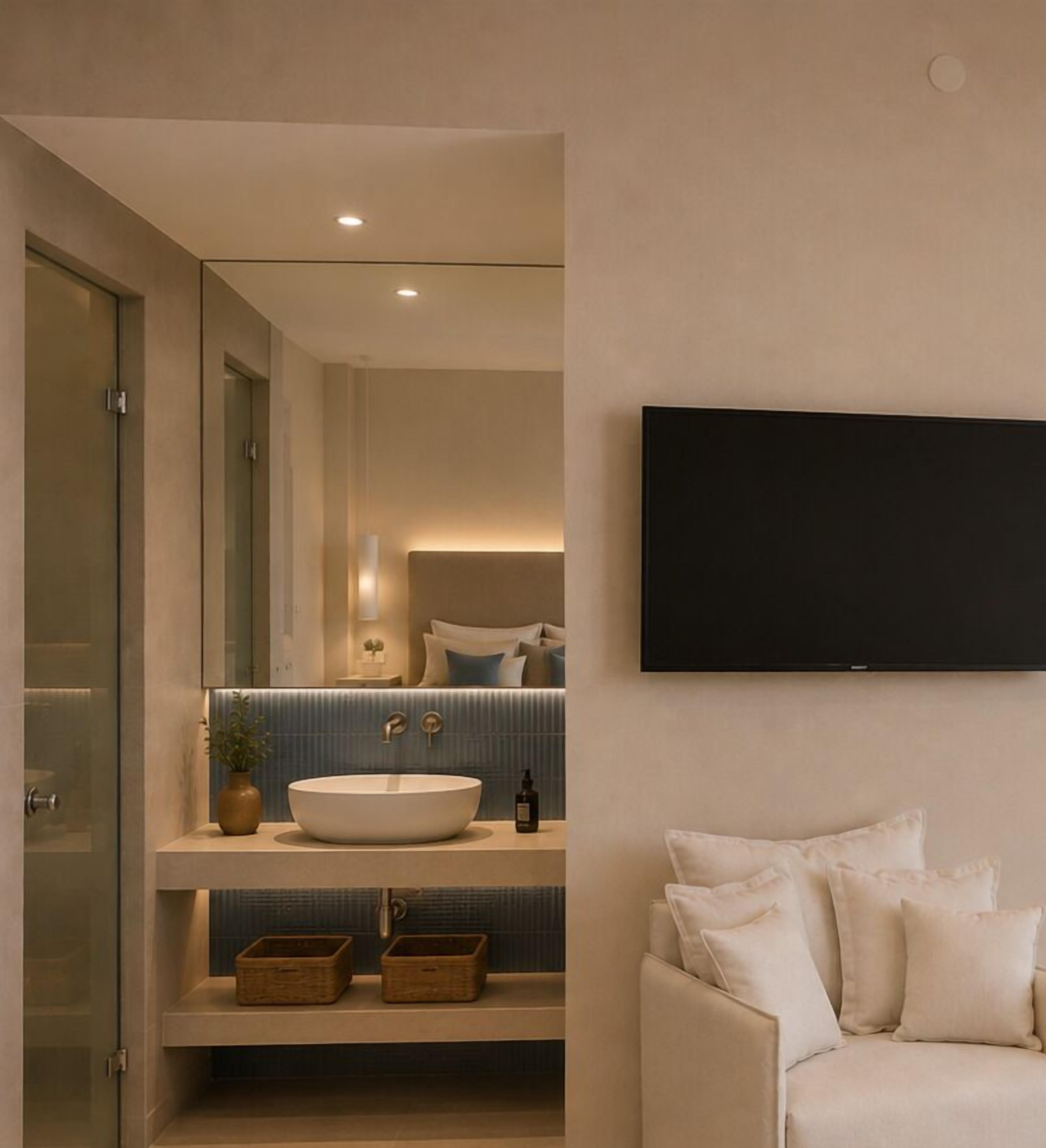 A modern bathroom with a large mirror, a white sink, and a flat-screen TV mounted on the wall.