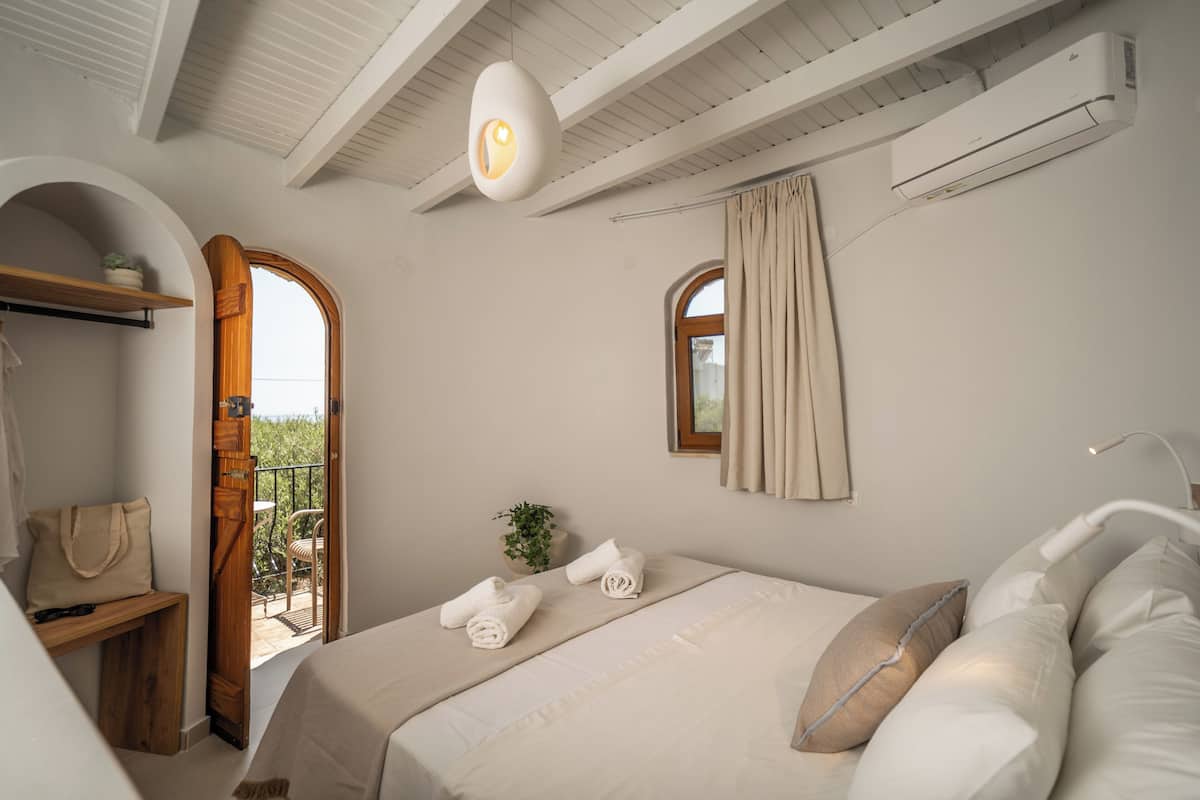 A bedroom with a bed, towels, a hanging light fixture, an air conditioning unit, and a window with curtains.