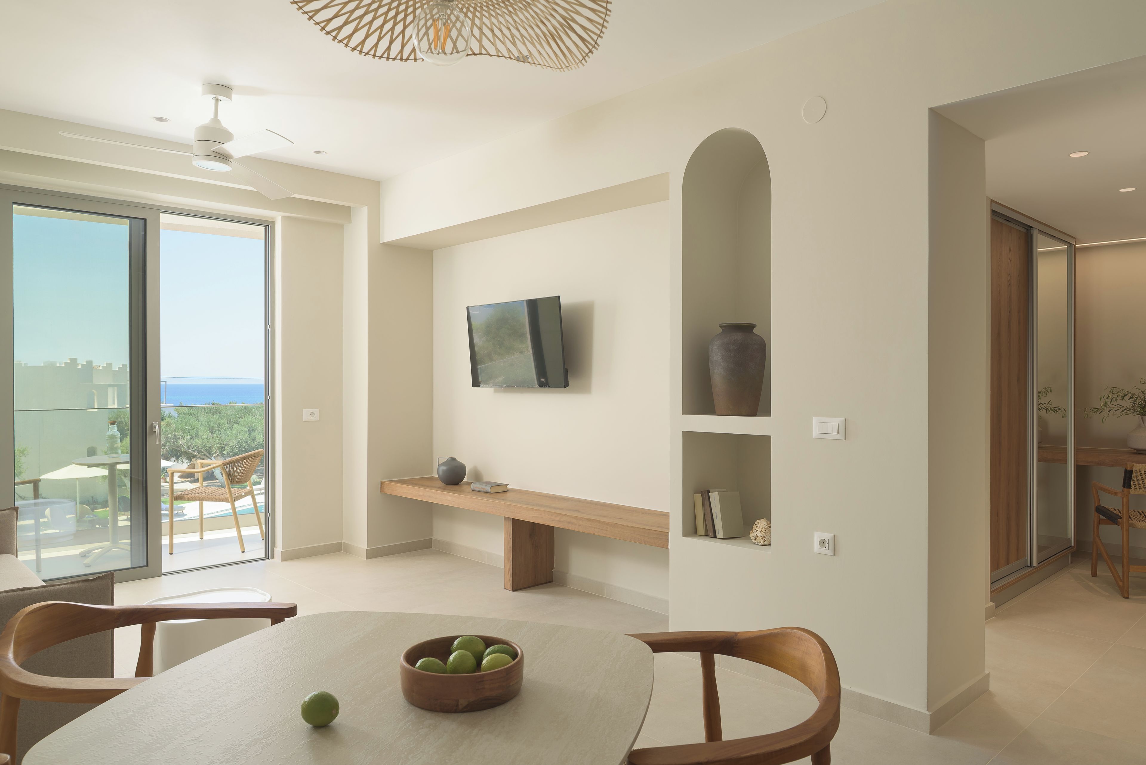 A modern interior with a dining area, a TV mounted on the wall, and a view of the outdoors.