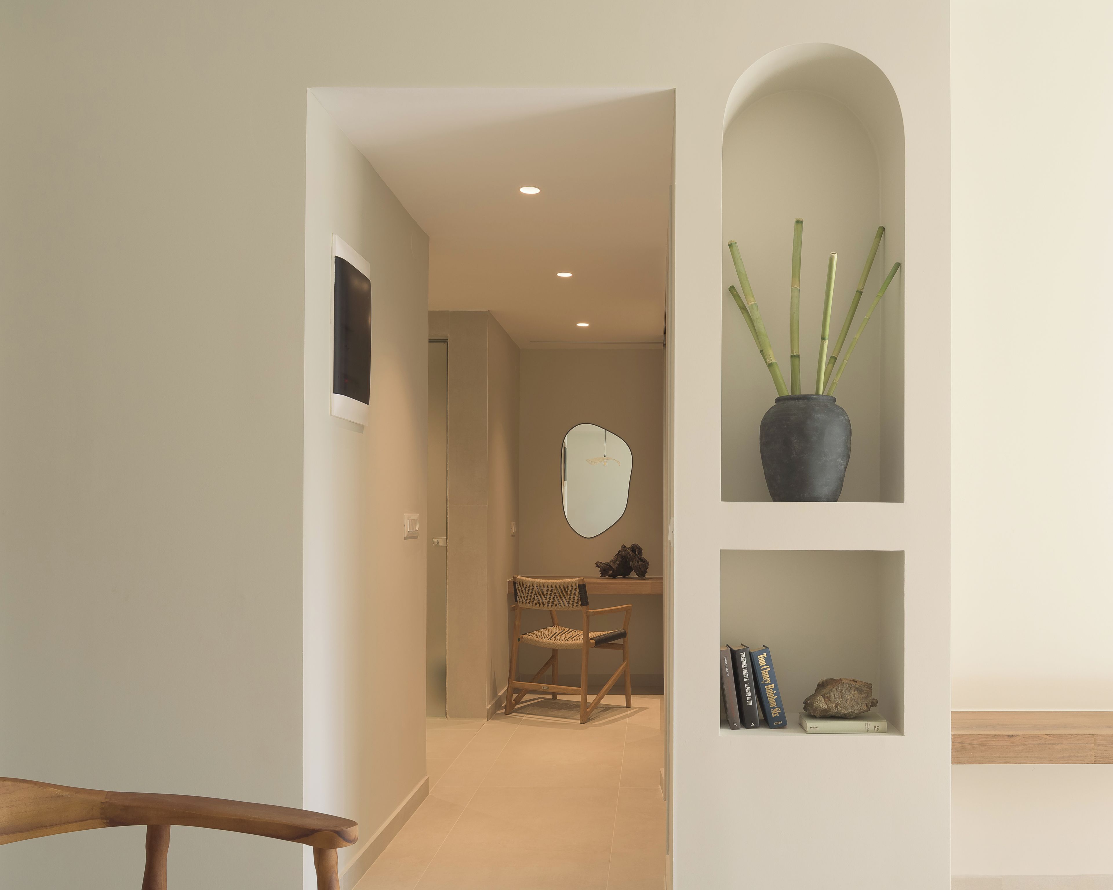A hallway with a wooden chair, a mirror, and a shelf with a potted plant.