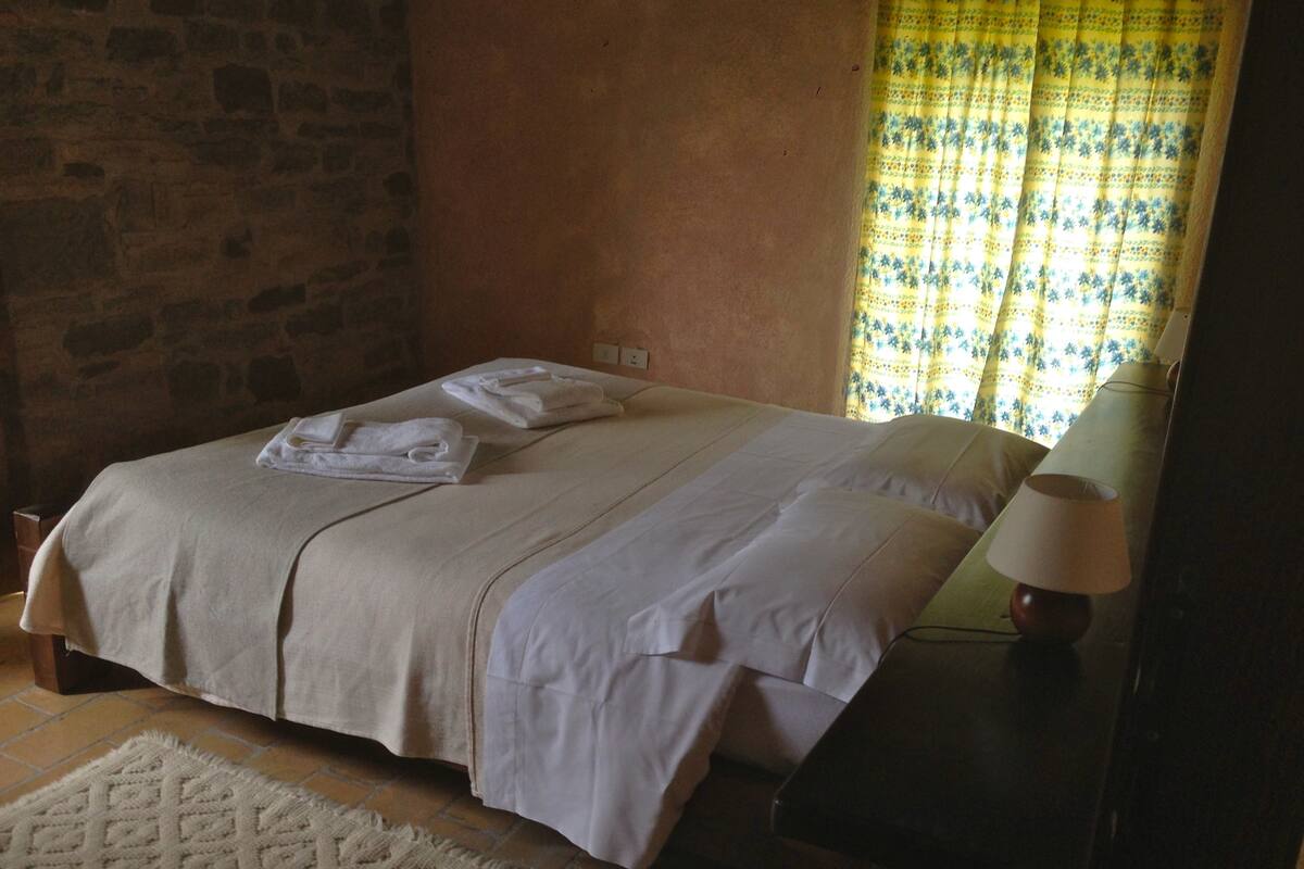 A bed with white linens, a bedside table with a lamp, and a patterned rug.