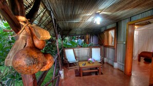 Um quarto rústico com teto de bambu, uma mesa de madeira com um vaso e uma planta grande ao fundo.