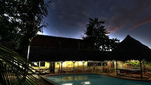 Uma área de piscina com espaço de estar coberto e um edifício ao fundo.