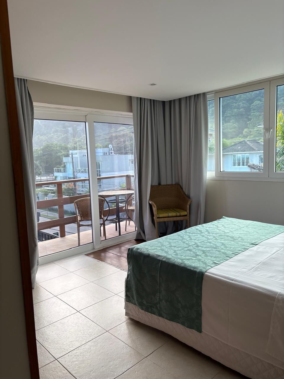 A bedroom with a bed, a chair, a balcony with a table, and a view of buildings.