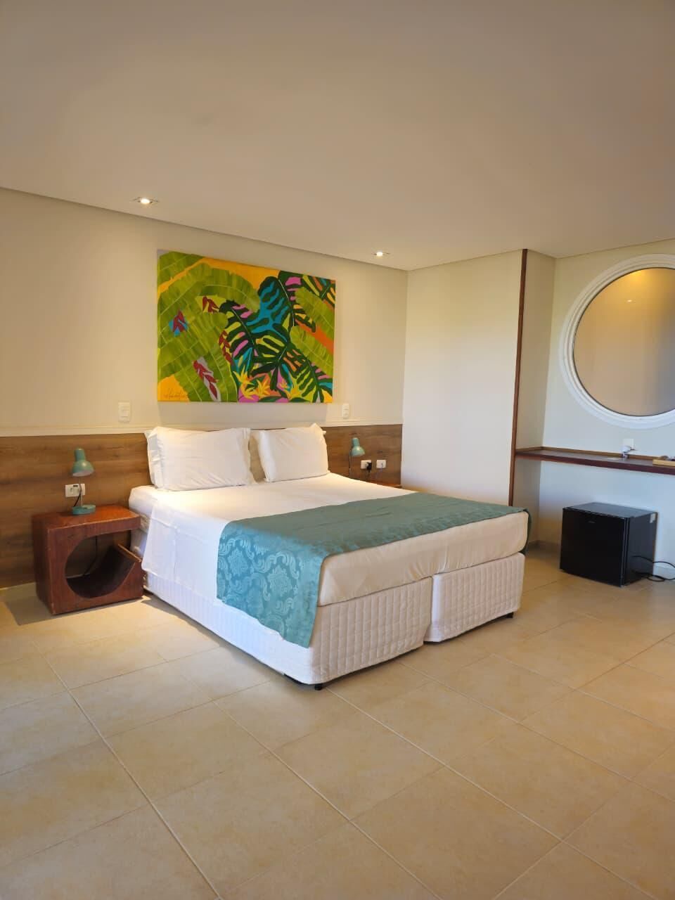 A neatly arranged bedroom with a bed, a bedside table, a small cabinet, and a wall-mounted circular mirror.
