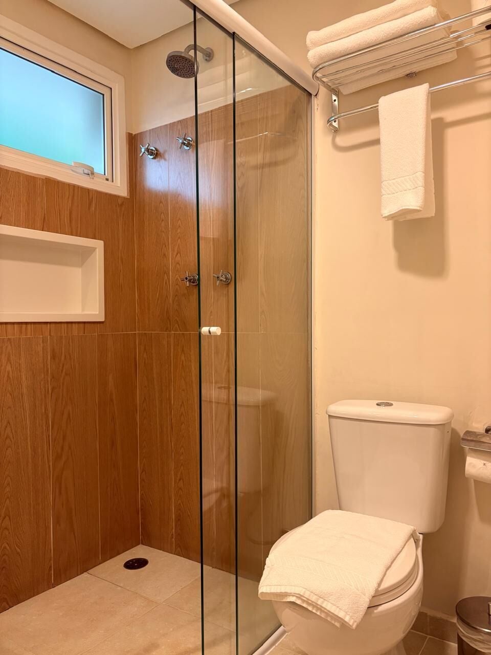 A bathroom with a glass-enclosed shower, a toilet, and a window.