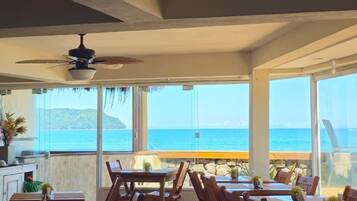 Un restaurante con mesas y sillas de madera, ventiladores de techo y vista al océano.