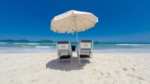 Two beach chairs with a beach umbrella on a sandy beach with a clear blue sky and ocean in the background. - Juquehy La Plage (São Sebastião)