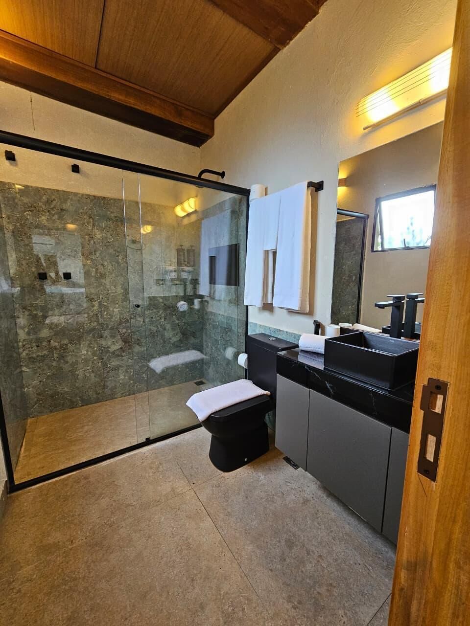 Une salle de bain moderne avec une douche à parois de verre, des toilettes, un lavabo doté d’un plan de travail noir et un miroir au-dessus du lavabo.