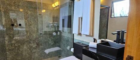 Une salle de bain moderne avec une douche à parois de verre, des toilettes, un lavabo doté d’un plan de travail noir et un miroir au-dessus du lavabo.