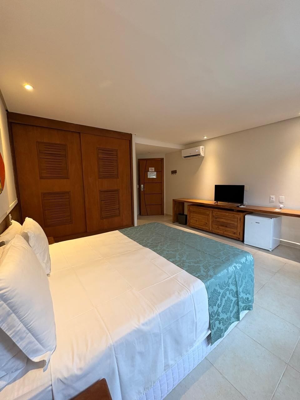 A hotel room with a bed, a desk, a television, and an air conditioning unit.