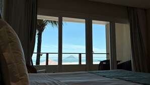 A bedroom with a bed, a view of the beach, and a large window. - Juquehy La Plage (São Sebastião)