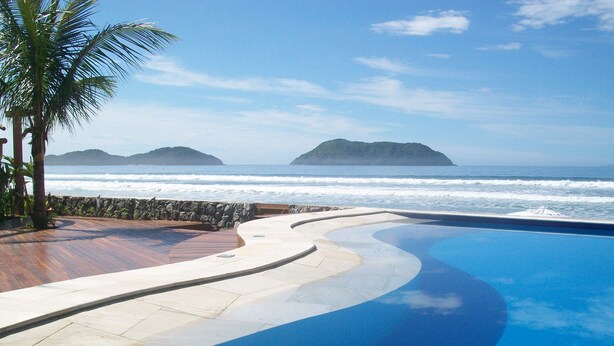 A curved infinity pool with a view of the ocean and distant islands. - Juquehy La Plage (São Sebastião)