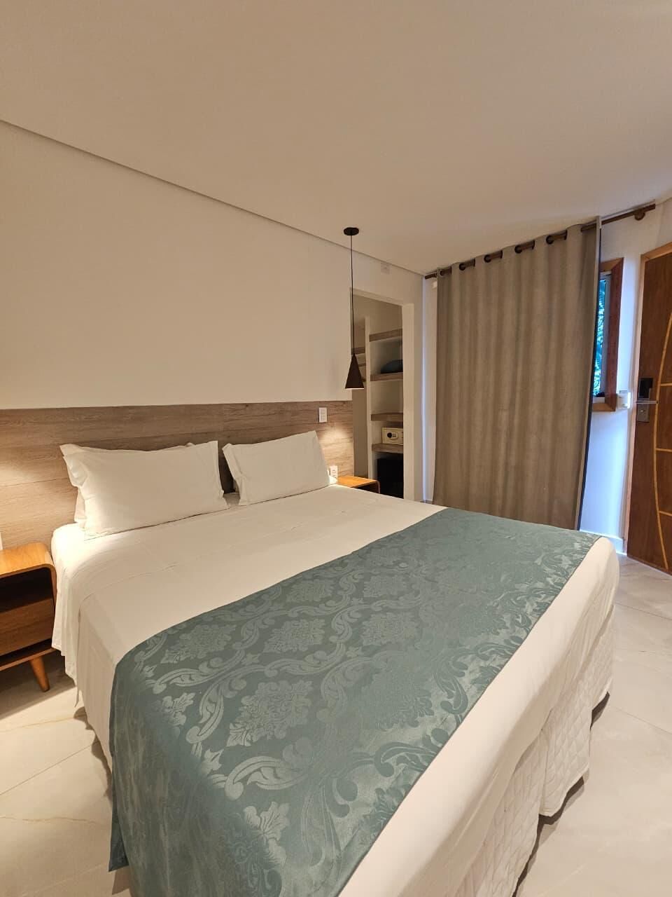 A modern hotel room with a large bed, a wooden headboard, a bedside table, and a built-in wardrobe.