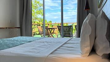 A bedroom with a large bed, a wooden nightstand, a hanging lamp, and a view of the outdoors.