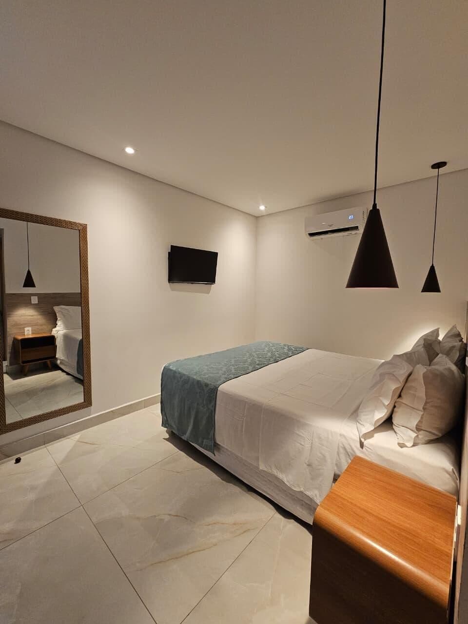 Un dormitorio moderno con cama, mesita de noche, espejo y televisor de pantalla plana.