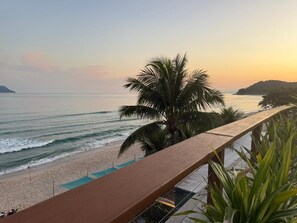 A beach view with a wooden railing, palm trees, and a calm sea. - Juquehy La Plage (São Sebastião)