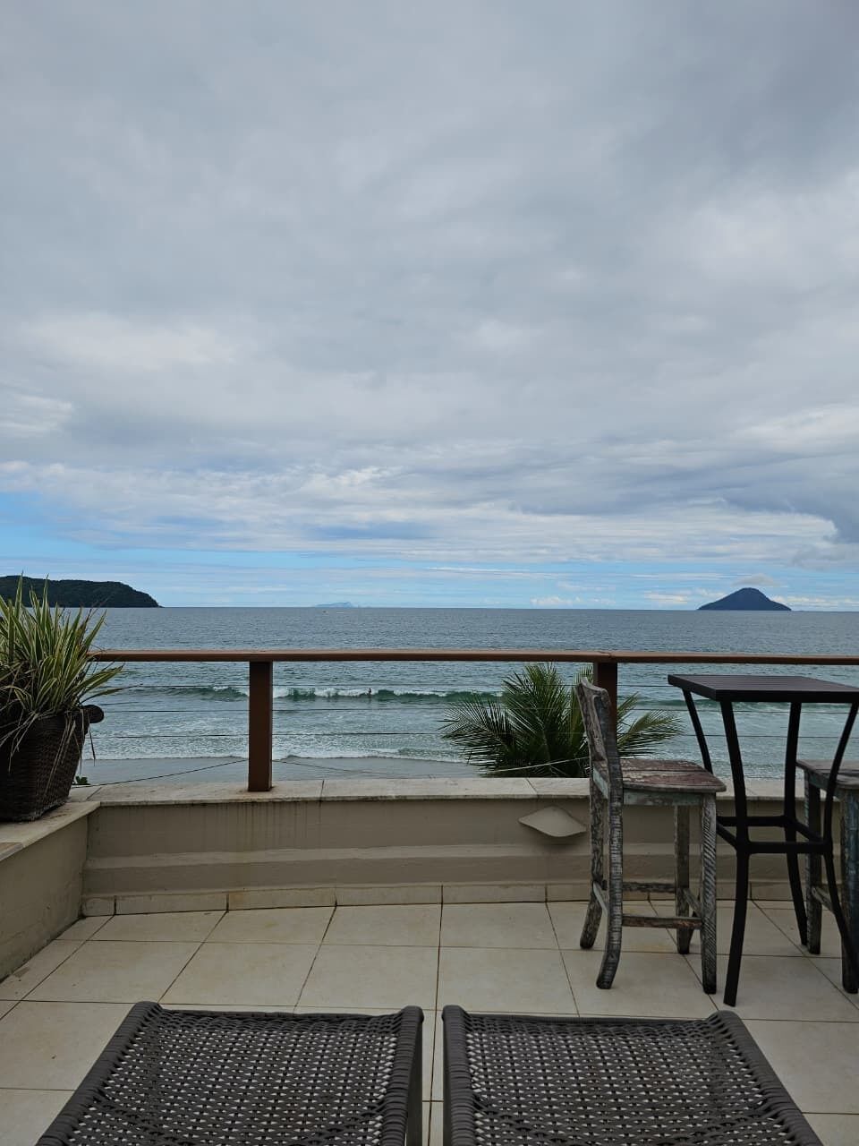 Un balcón con vista al mar, una silla y una mesa.