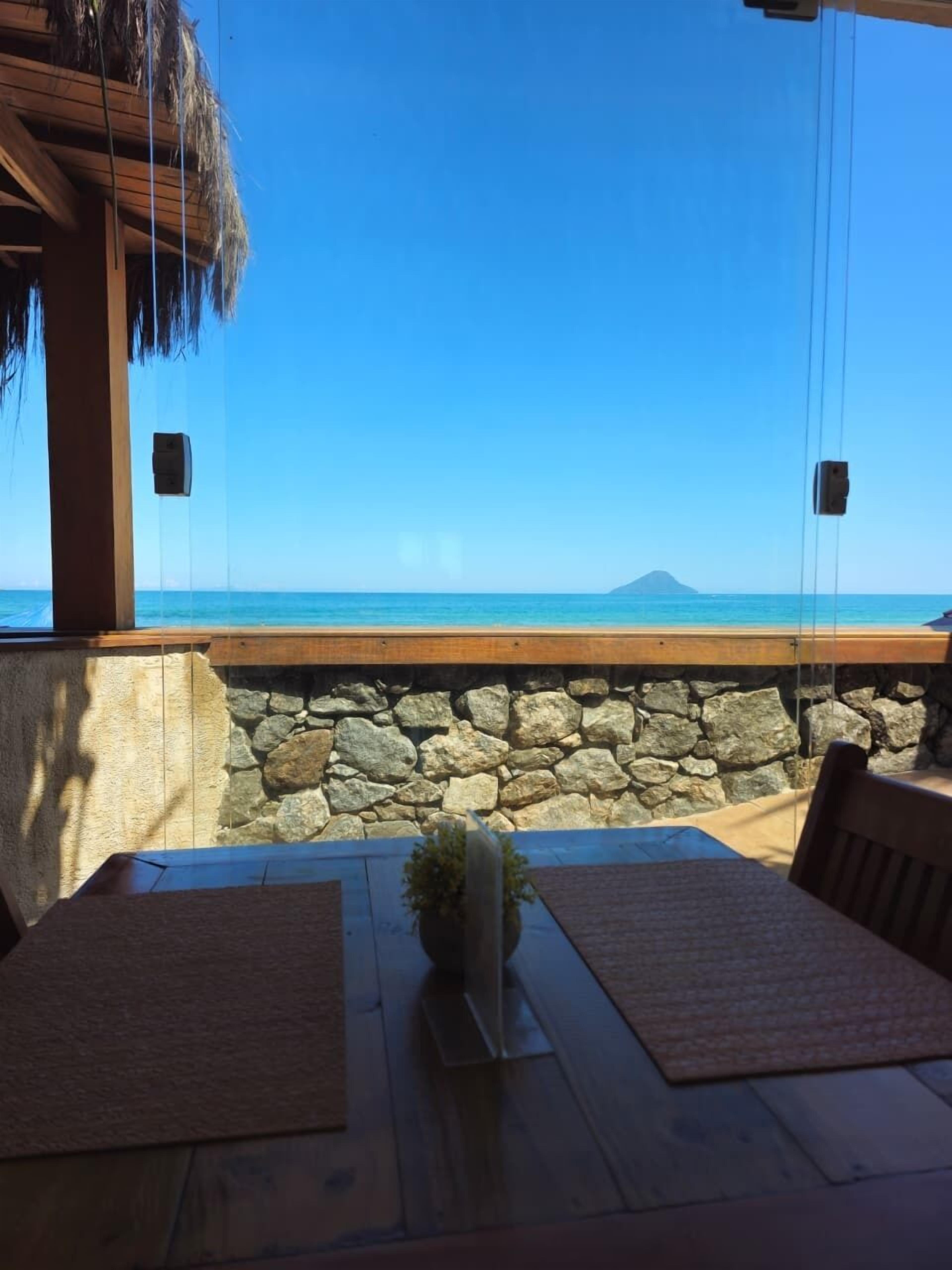 Una mesa de madera con un centro de mesa de planta, una pared de piedra y vista al océano.