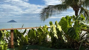 A patio with two black mesh lounge chairs, a wooden deck, and a view of the ocean with a distant island. - Juquehy La Plage (São Sebastião)