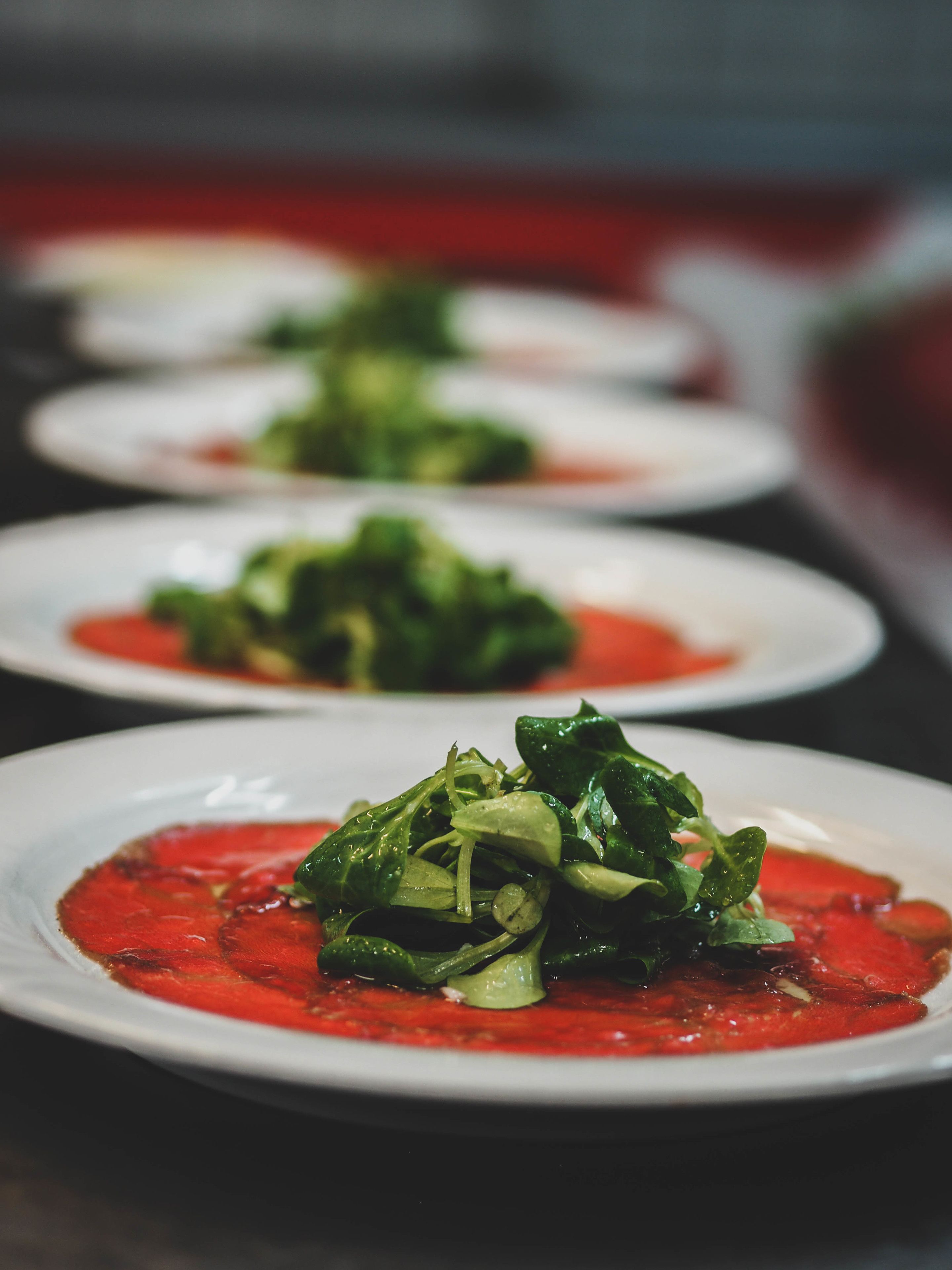 Una hilera de platos blancos con salsa roja y verduras de hoja verde.