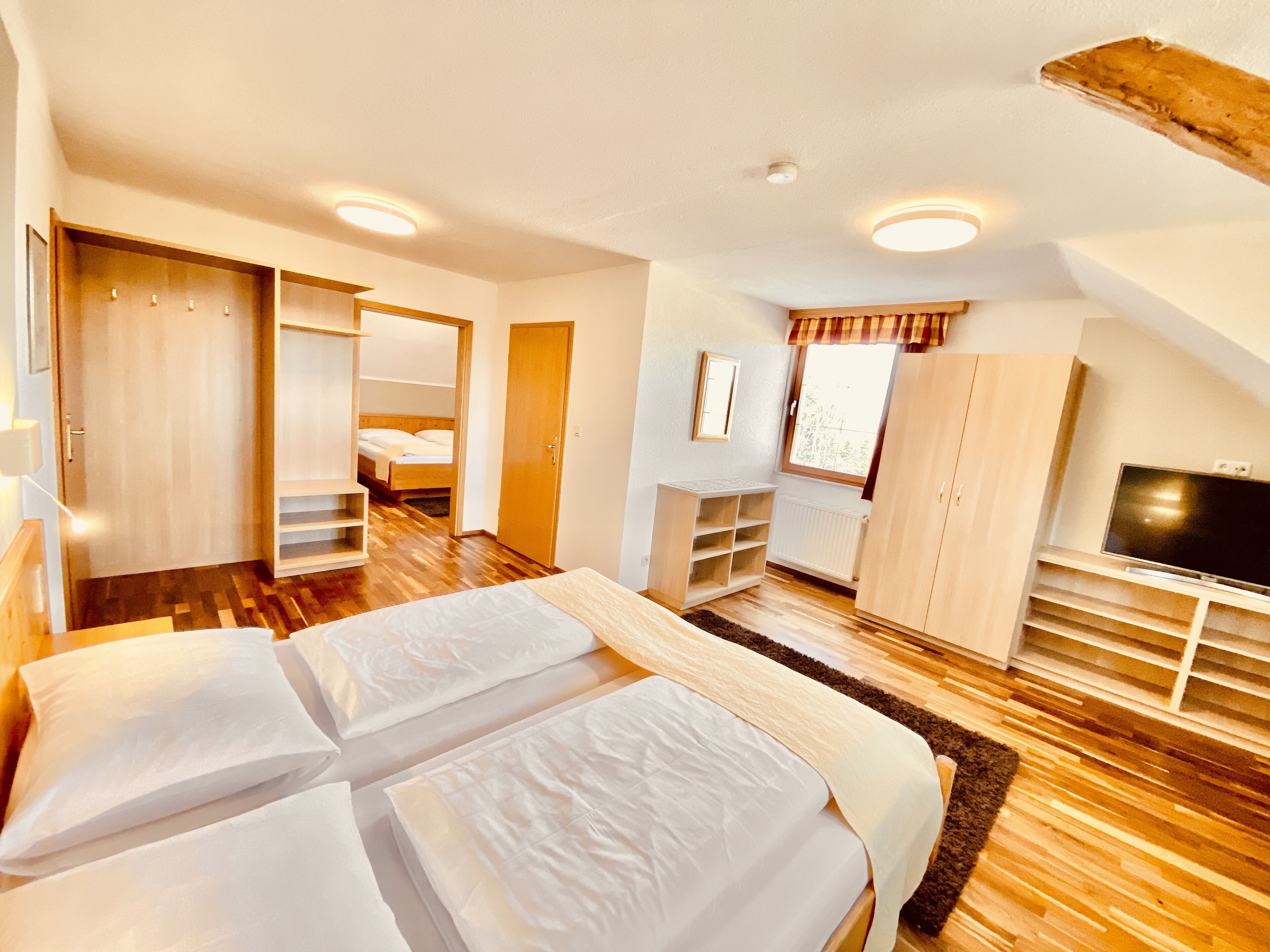 A bedroom with two beds, a TV, a wardrobe, and a window with curtains.