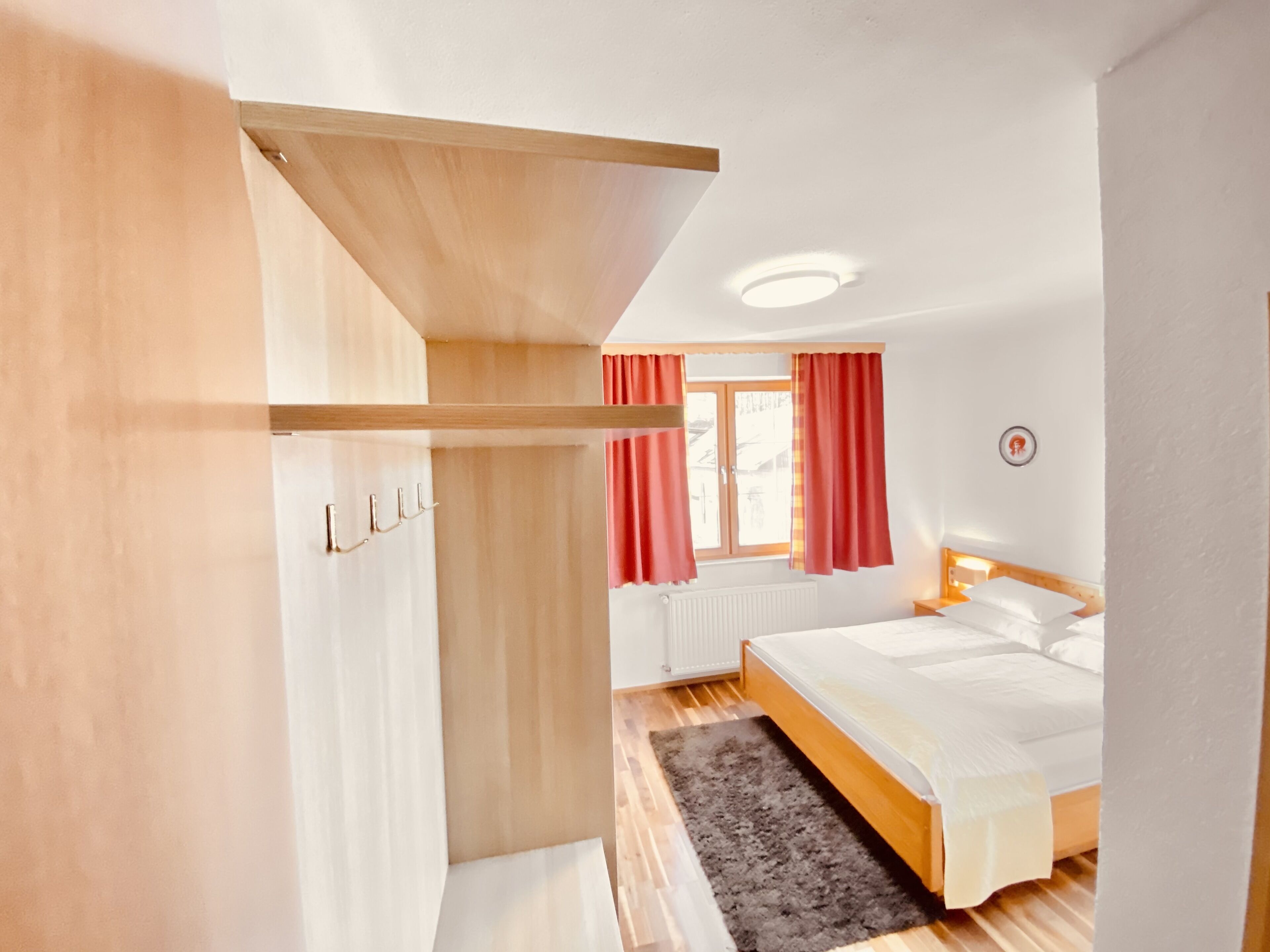 Une chambre à coucher avec un lit, une armoire en bois, un radiateur et une fenêtre avec des rideaux rouges.