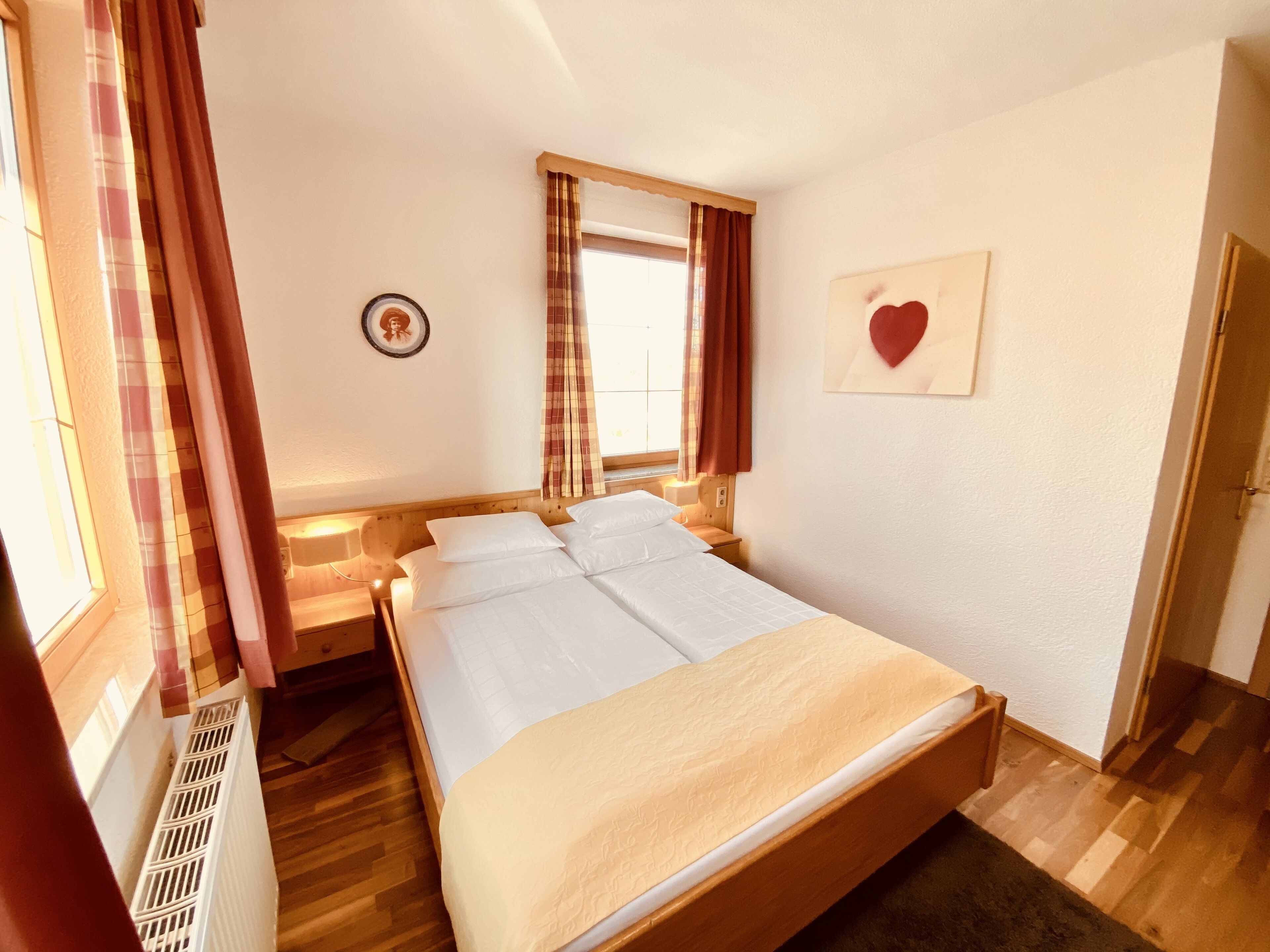 Ein ordentlich bezogenes Bett mit weißen Leinen, einem hölzernen Kopfteil und einem Fenster mit Vorhängen.