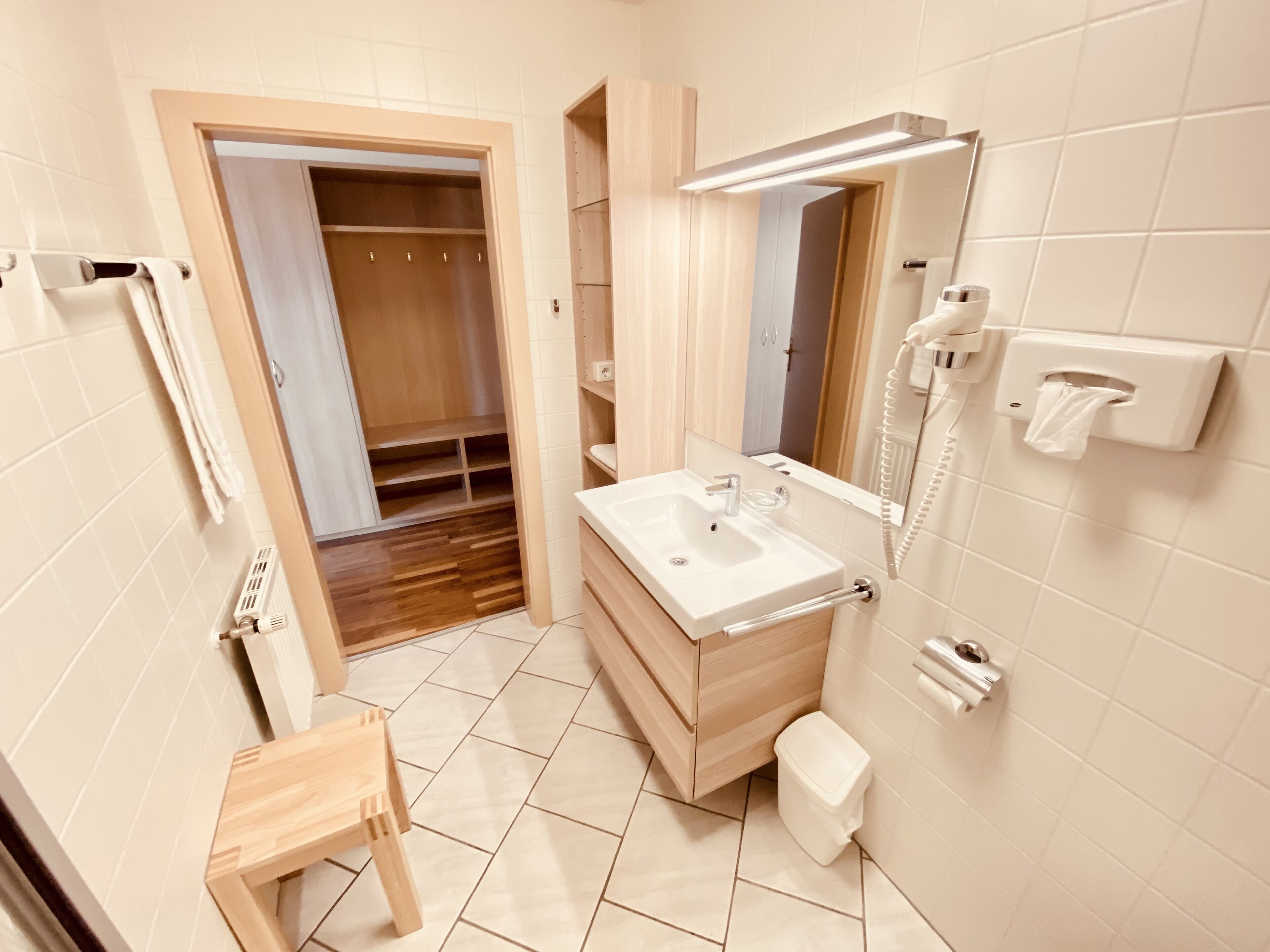 Un bagno moderno con un mobile vanitario in legno, un lavandino, uno specchio, un dispenser di asciugamani e un water.