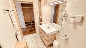 Un bagno moderno con un mobile vanitario in legno, un lavandino, uno specchio, un dispenser di asciugamani e un water.